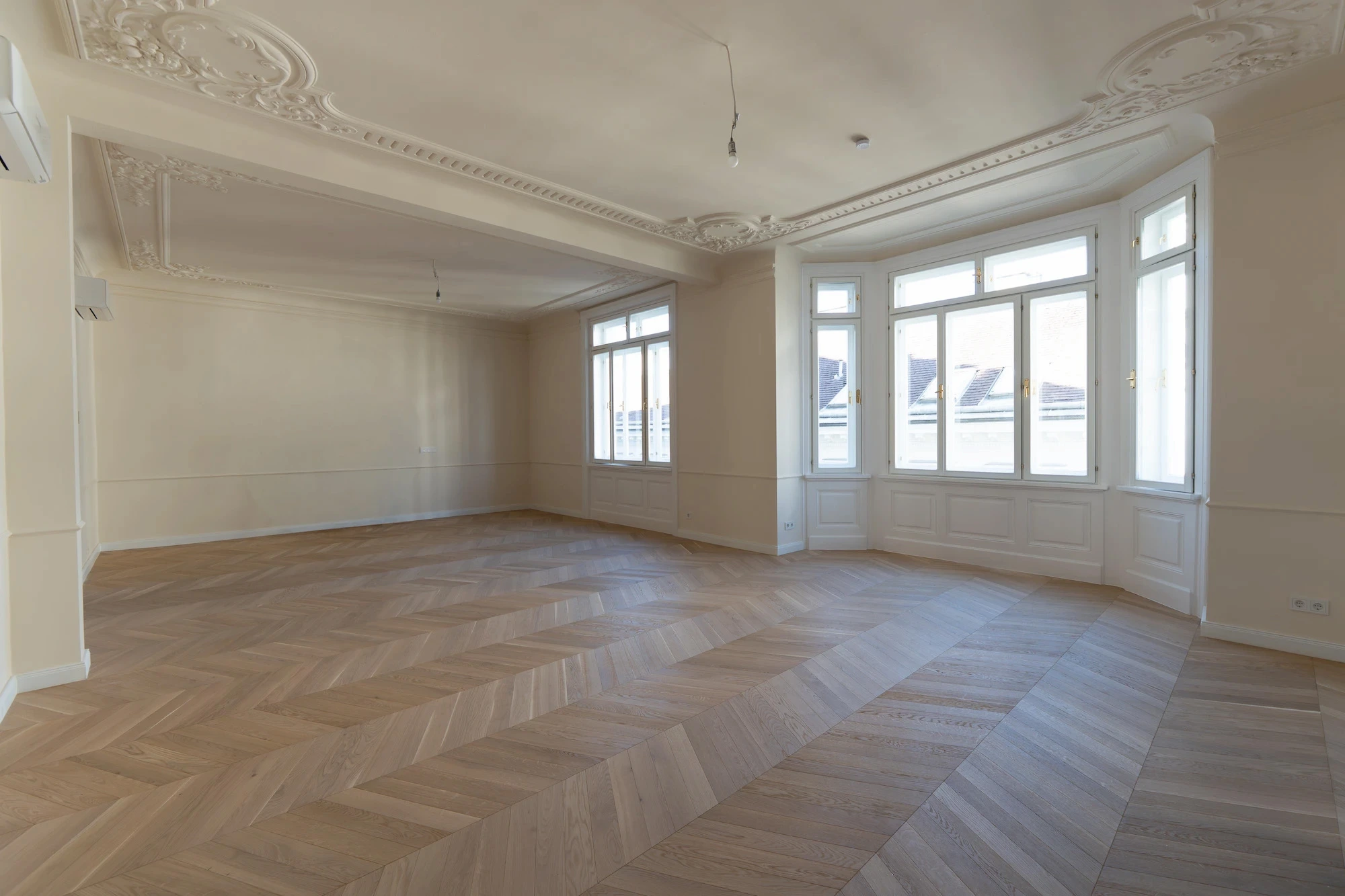 Großzügiger Wohnraum einer sanierten Altbauwohnung in Wien mit Fensterfront und Fischgrätparkett