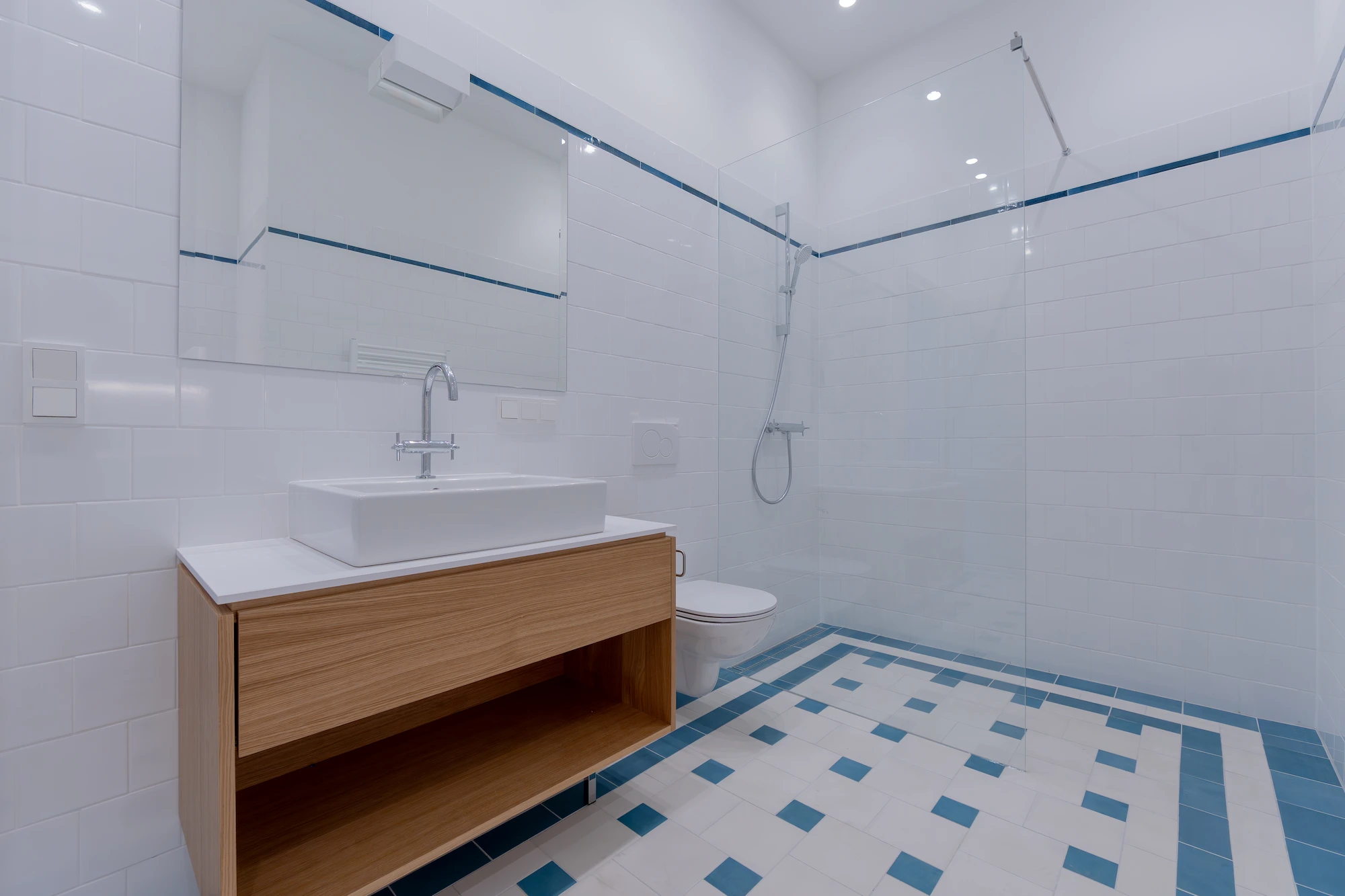 Badezimmer mit Dusche, Waschtisch und blau akzentuiertem Fliesenboden