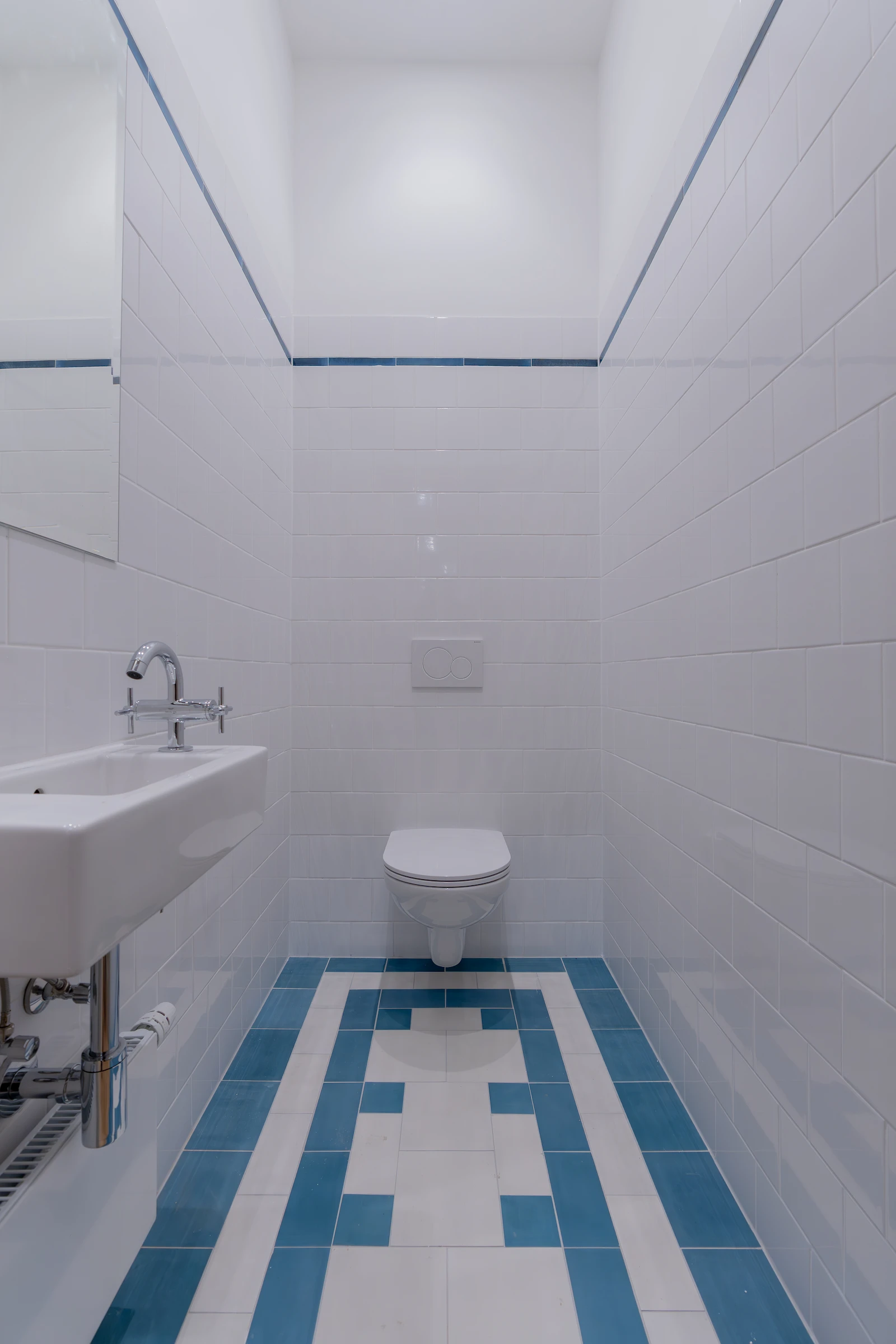 Gäste-WC mit weißer Wandgestaltung und blau akzentuiertem Fliesenboden