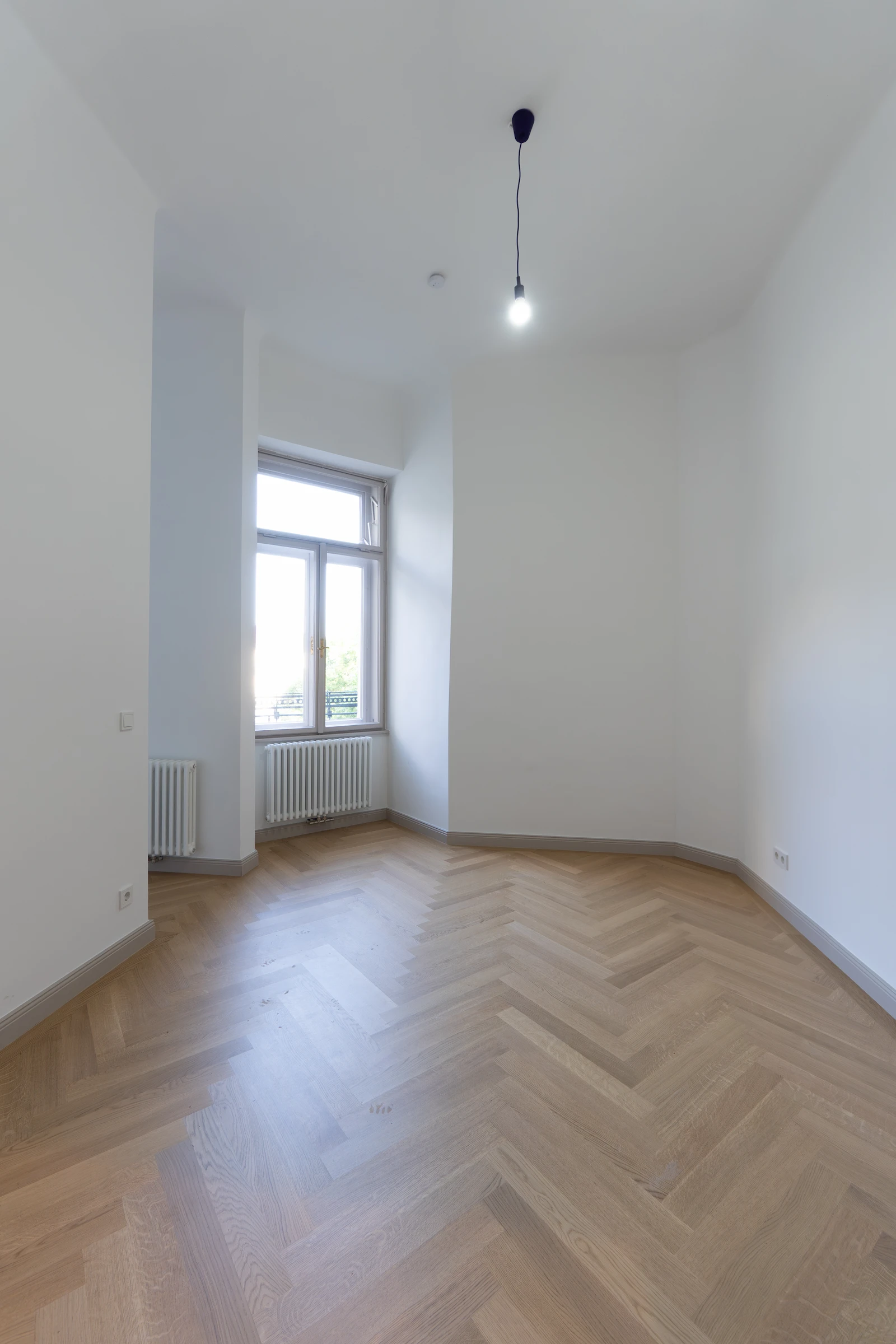 Schmales helles Zimmer mit Fischgrätparkett und Fenster