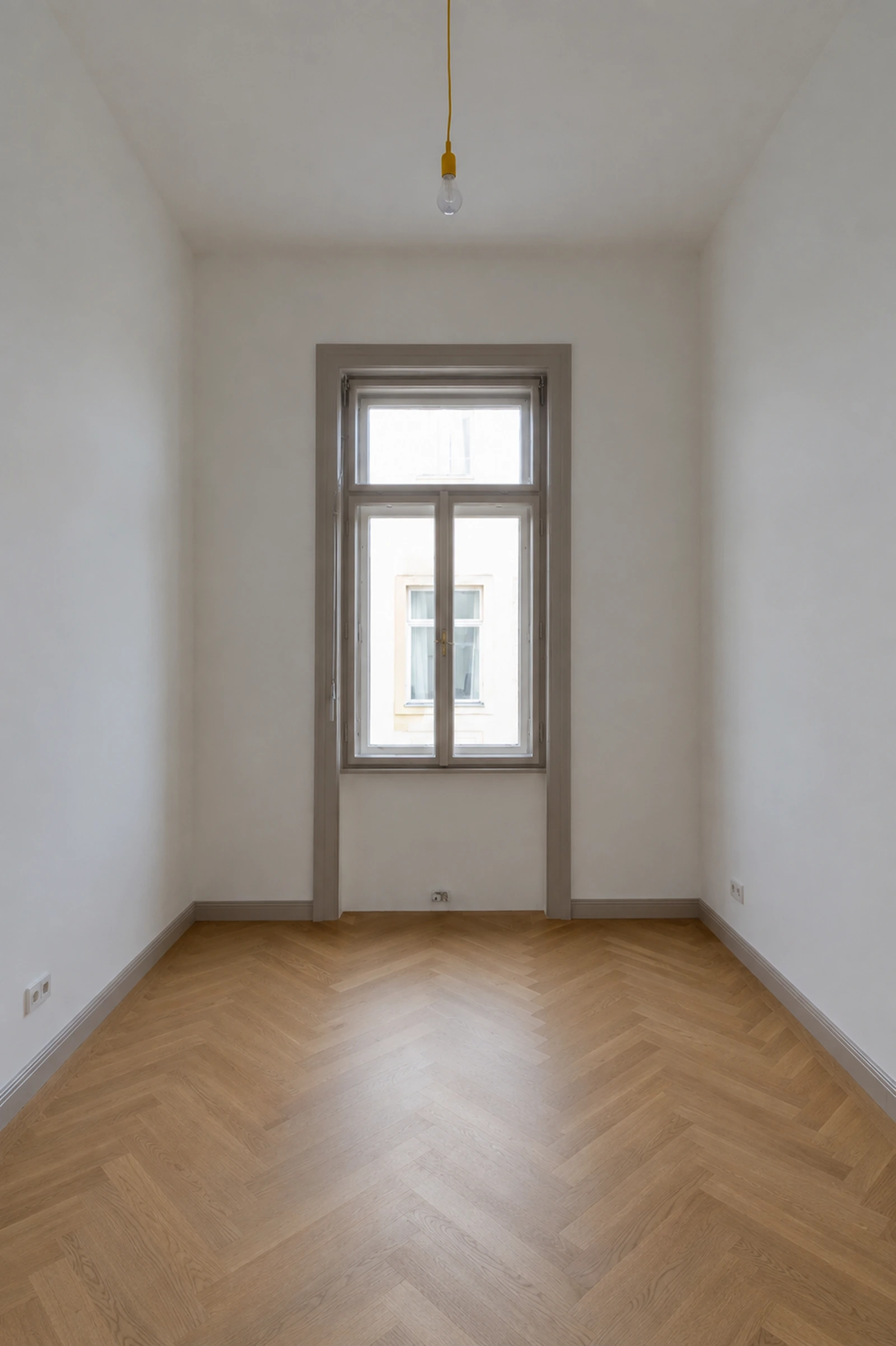 Schmales Altbauzimmer mit Fischgrätparkett und hoher Fensteröffnung